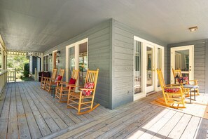 A covered porch with wooden rocking chairs and a table, a sliding glass door, and a small light fixture.