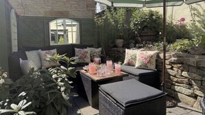 En patio med fletmøbler, et bord med drikkevarer og en stribet parasol.