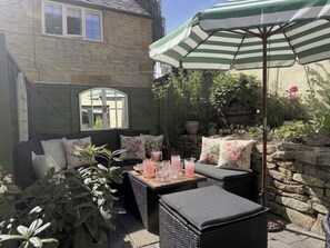 Eine Terrasse mit Korbmöbeln, einem Tisch mit Getränken und einem gestreiften Sonnenschirm.