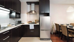 A modern kitchen with dark cabinetry, a stainless steel refrigerator, and a dining area with wooden chairs and a table. - 57m²Clean&Quiet/1GbWiFi/Kingbed/Cook/BalconyWasher (Watthana)