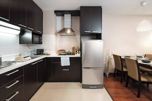 Eine moderne Küche mit dunklen Schränken, einem Edelstahlkühlschrank und einem Essbereich mit Holztischen und einer Tischplatte.
