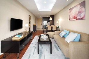 Ein modernes Wohnzimmer mit Flachbildfernseher, Couchtisch, einer Couch mit Kissen und einem Essbereich mit Stühlen.