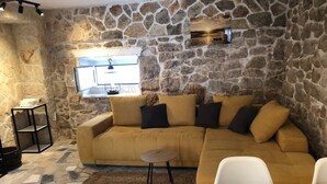 A cozy living area with a stone wall, a sofa, a small table, and a window. - Mala kuca od soli / Whole house for a dream vacation (Jezera)