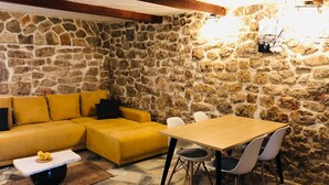 A stone-walled room with a yellow sofa, a wooden table with chairs, and a small table with a decorative item. - Mala kuca od soli / Whole house for a dream vacation (Jezera)