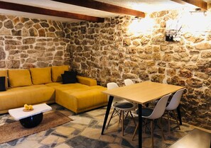 Ein Zimmer mit Steinwänden, einem gelben Sofa, einem Holztisch mit Stühlen und einem kleinen Tisch mit einem dekorativen Gegenstand.