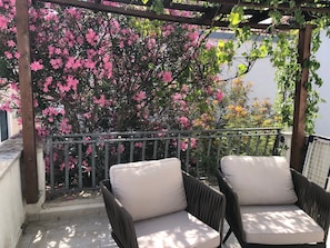 A balcony with two wicker chairs and a pergola with pink flowering trees. - Mala kuca od soli / Whole house for a dream vacation (Jezera)