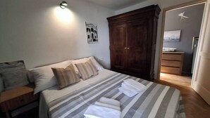 A neatly made bed with striped bedding and pillows, a wooden wardrobe, and a wall-mounted light fixture. - Mala kuca od soli / Whole house for a dream vacation (Jezera)