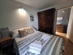 Ein ordentlich bezogenes Bett mit gestreifter Bettwäsche und Kissen, ein Holzschrank und eine wandmontierte Lampe.