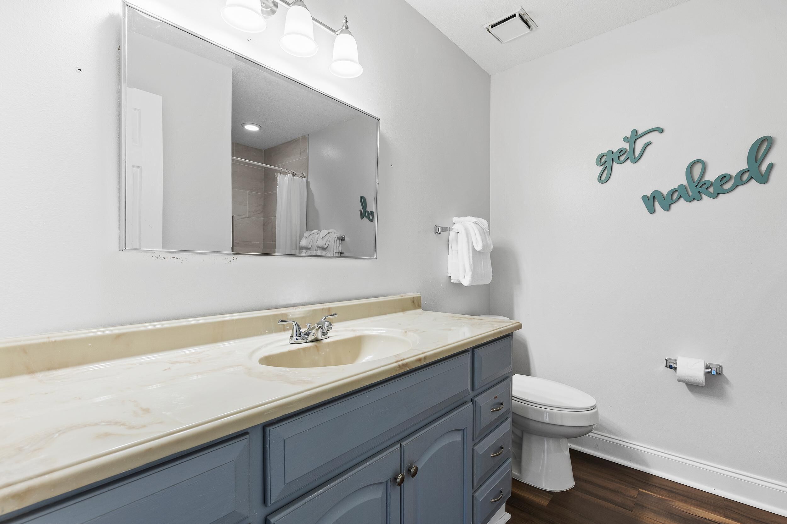 A bathroom with a double sink vanity, a toilet, and a mirror with lights.