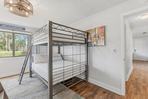 A bunk bed with a ladder, a window with a view of greenery, and a painting on the wall.