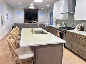 A modern kitchen with a large island, built-in appliances, and a seating area with wicker chairs.
