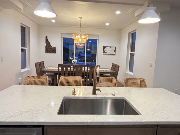 A kitchen with a large island, stainless steel sink, and pendant lighting.