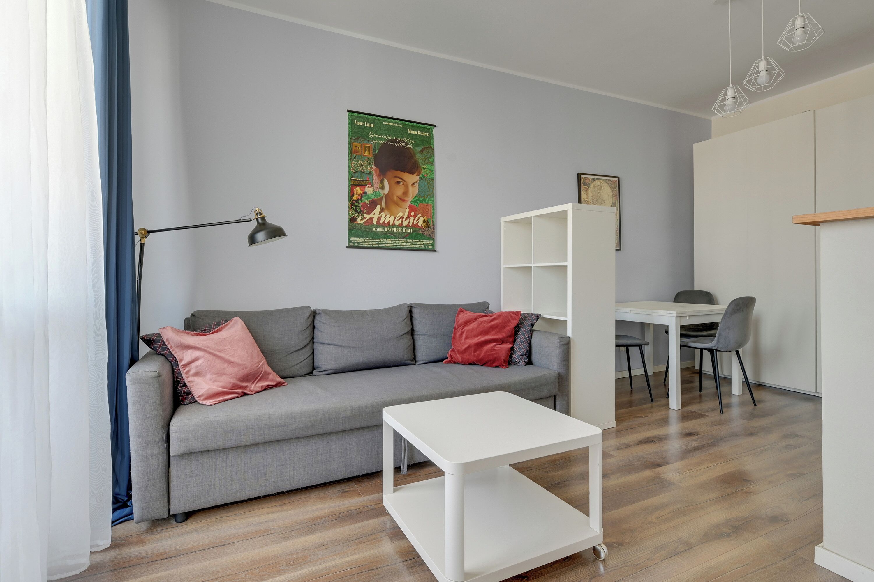A modern living room with a grey sofa, a white coffee table, and a dining area with a white table and chairs.