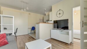 A compact living space with a kitchenette, a TV, a dining area, and a bed. - Abrahama 36 - by Grand Apartments (Gdynia)