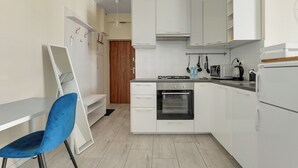 A modern kitchen with white cabinets, a stove, oven, and a blue chair. - Abrahama 36 - by Grand Apartments (Gdynia)