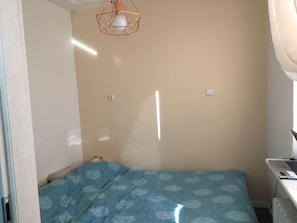 Ein Schlafzimmer mit einem Bett, einem Schreibtisch mit Laptop, einer Steckdose und einer Deckenleuchte.