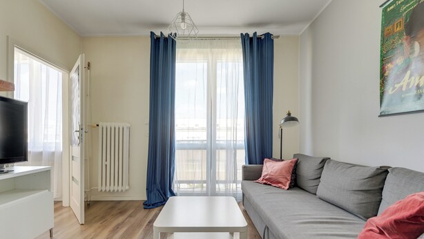 A living room with a white coffee table, grey sofa, and a television on a white stand. - Abrahama 36 - by Grand Apartments (Gdynia)