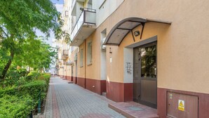 A building with a red and beige facade, a gated entrance, and a paved walkway. - Abrahama 36 - by Grand Apartments (Gdynia)