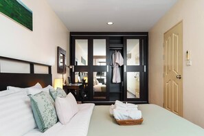 Habitación de hotel con una cama, un escritorio con una computadora portátil, una bata colgada y vistas a través de una puerta de cristal.