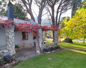 A stone house with a covered porch, a stone chimney, and a well-maintained garden with a lawn and trees.