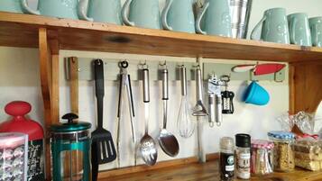 Un estante de cocina con varios utensilios, una prensa francesa y frascos de especias.