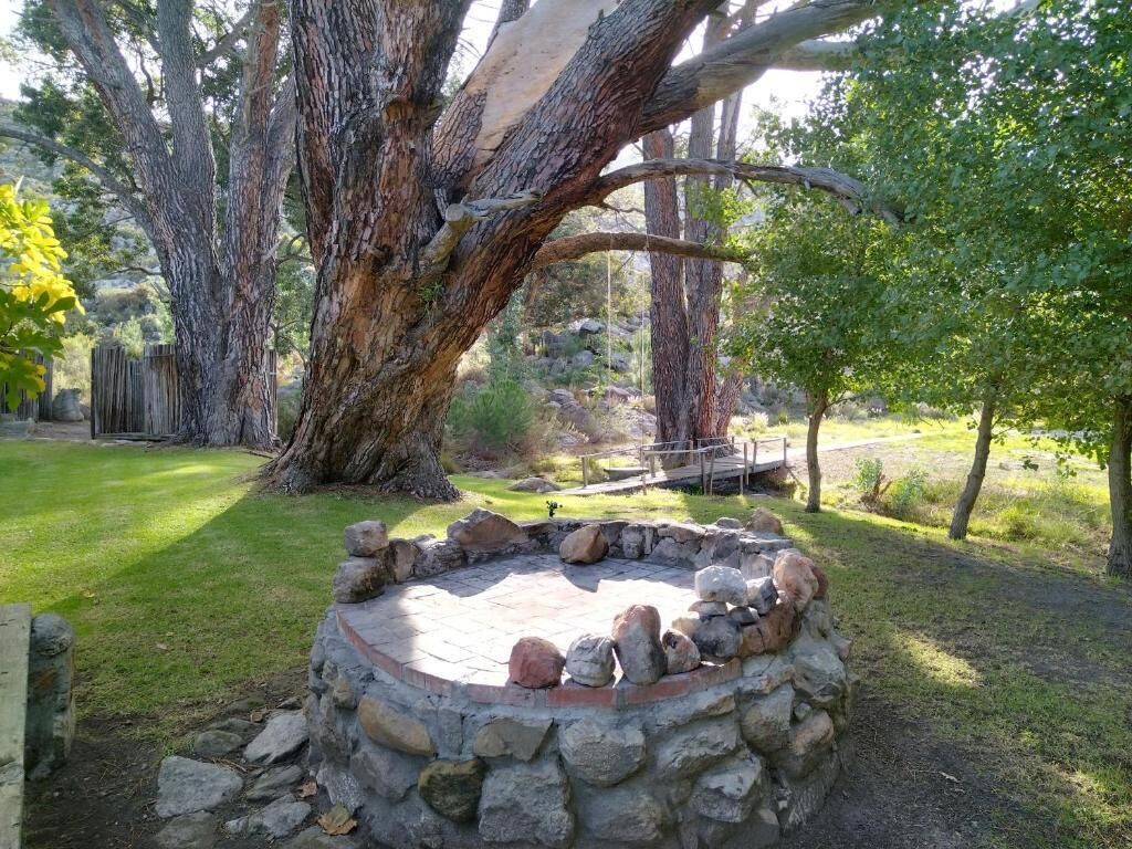 Un pozo de fuego de piedra rodeado por un muro de piedra, con un banco de madera y una cerca de madera al fondo.