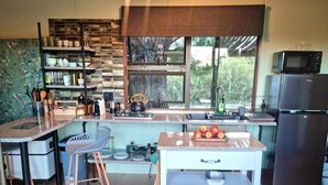 A compact kitchen with a central island, a microwave, a refrigerator, and a window with a view of greenery. - Fairfield Cottages (Ceres)