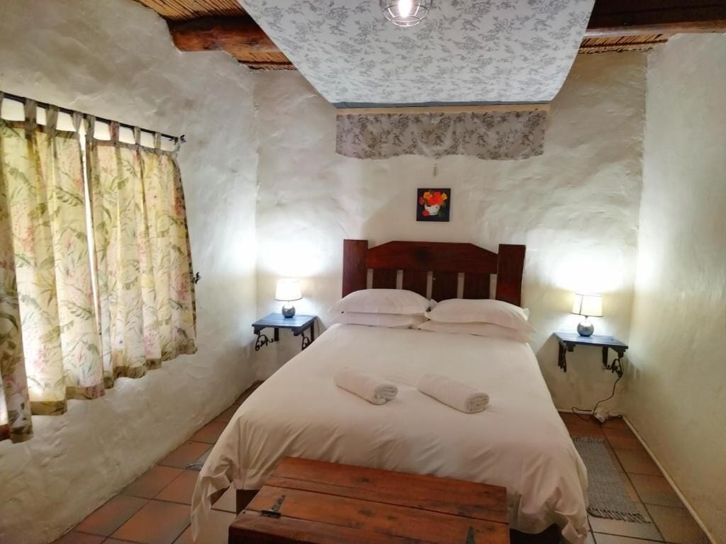 Un dormitorio con cama, dos lámparas de noche, un banco de madera, una cortina floral y un aplique de techo.