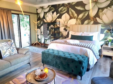 A bedroom with a large bed, a sofa, a coffee table, and a wall with a floral mural.. Fairfield Cottages
