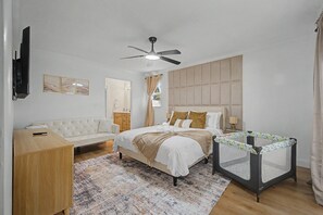 A bedroom with a bed, a ceiling fan, a TV, a bedside table, a dresser, a crib, and a patterned rug. - Splash & Relax Games•PedalBoat•Adventures•Lakeside (Royal Palm Beach)