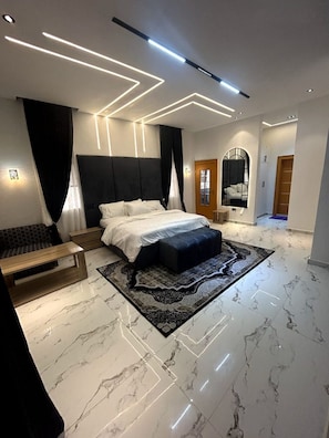 A modern bedroom with a large bed, a bedside table, a bench, a mirror, and a patterned rug.