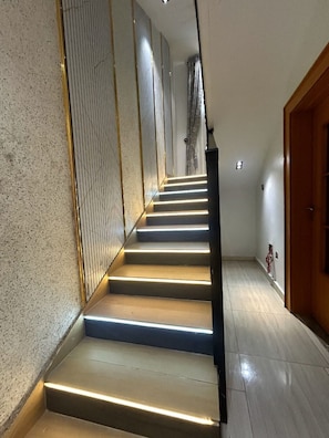 A staircase with illuminated steps leading to a landing, a wooden door on the right, and a textured wall on the left.