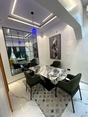 A modern conference room with a marble table, green chairs, a large mirror, and a contemporary light fixture.