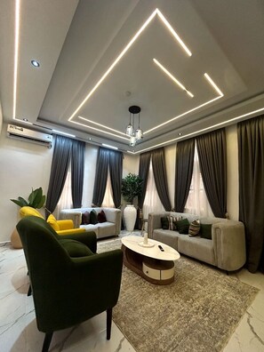 A modern living room with a sofa, armchair, and coffee table, featuring a geometric ceiling design and a large vase.