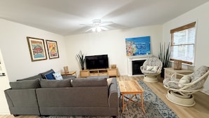 Ein Wohnzimmer mit grauem Sofa, Fernseher, Kamin und Deckenventilator.