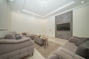 A living room with a sofa set, a coffee table, and a TV mounted on the wall. - 2-BR apart. in Al Marwa /10 Mins away from Airport (Jeddah)