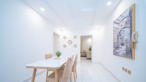 Uma sala de jantar moderna com uma mesa branca, cadeiras bege e uma pintura representando uma cena de canal.