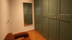 Een kamer met een houten vloer met een mozaïekpatroon, een grote spiegel en een garderobe met meerdere deuren.