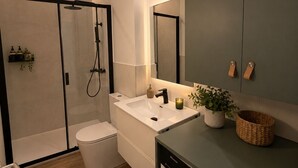 Een moderne badkamer met een douchecabine van glas, een wit toilet, een wastafel met spiegel en een wasmachine.