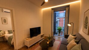Een moderne woonkamer met een flatscreen televisie, een plafondventilator, een bank, een salontafel en een balkon met uitzicht.