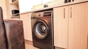 Una cocina moderna con lavadora y secadora integradas de acero inoxidable, armarios de madera y piso de baldosas.