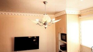 Una habitación con candelabro, televisión de pantalla plana, armarios de madera y una ventana.