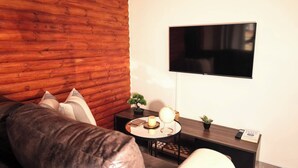 Una sala de estar con una pared de madera, un sofá, una mesita de centro con un globo terráqueo y libros, y un televisor montado en la pared.