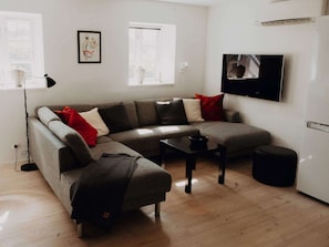 Ein modernes Wohnzimmer mit einem grauen Ecksofa, einem kleinen schwarzen Tisch und einem weißen Schrank.
