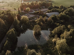 Eine Vogelperspektive auf ein Anwesen mit einem zentralen Wasserspiel, umgeben von dichten Bäumen, einem Parkplatz und einem kleinen Gebäude mit Satteldach.