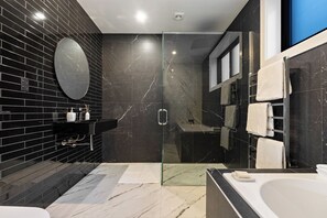 Une salle de bain moderne avec une douche à parois de verre, un mur recouvert de carreaux de marbre, un miroir rond et une baignoire blanche.