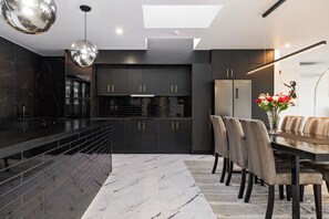 Une cuisine moderne avec des meubles de couleur sombre, un plan de travail en marbre et un coin repas comprenant une table et des chaises.