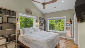 Quarto com cama, estantes, ventilador de teto e janelas amplas.