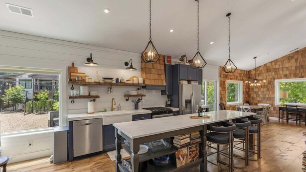 Uma cozinha moderna com ilha central, banquetas e iluminação pendente.