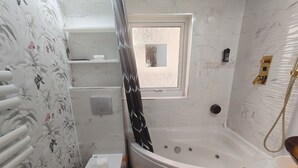 Et badeværelse med badekar, toilet, bruser og et vindue.